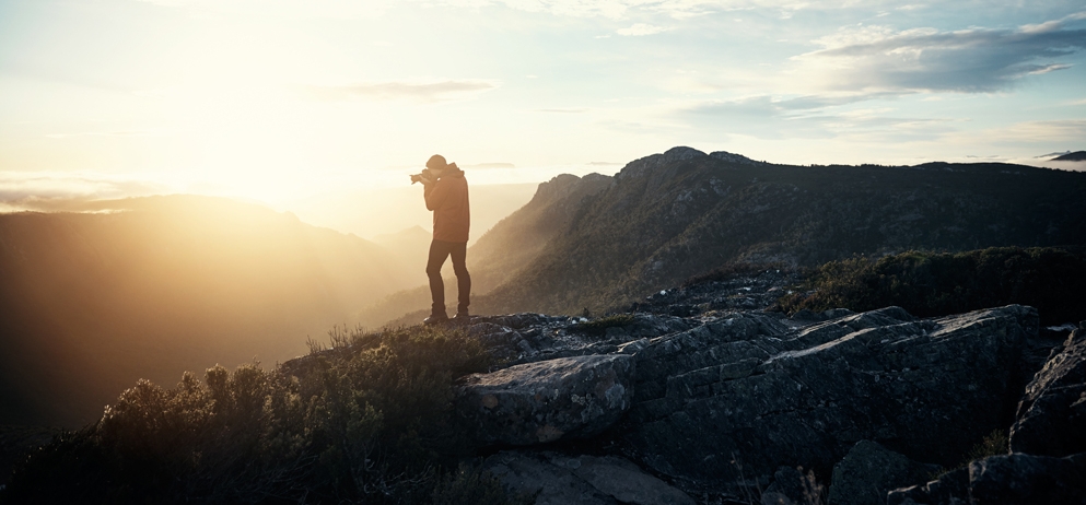 person stands on top of a mountain while taking a photo