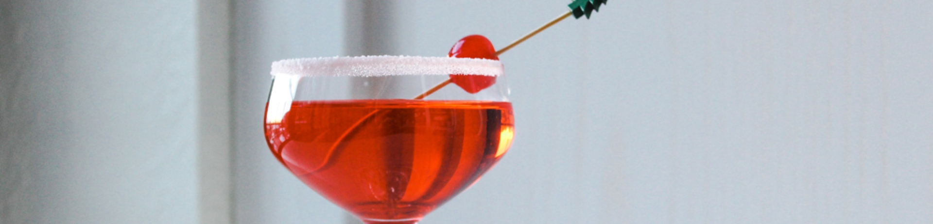 a red coloured drink in a coupe glass with a cherry garnish