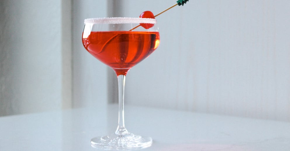 a red coloured drink in a coupe glass with a cherry garnish