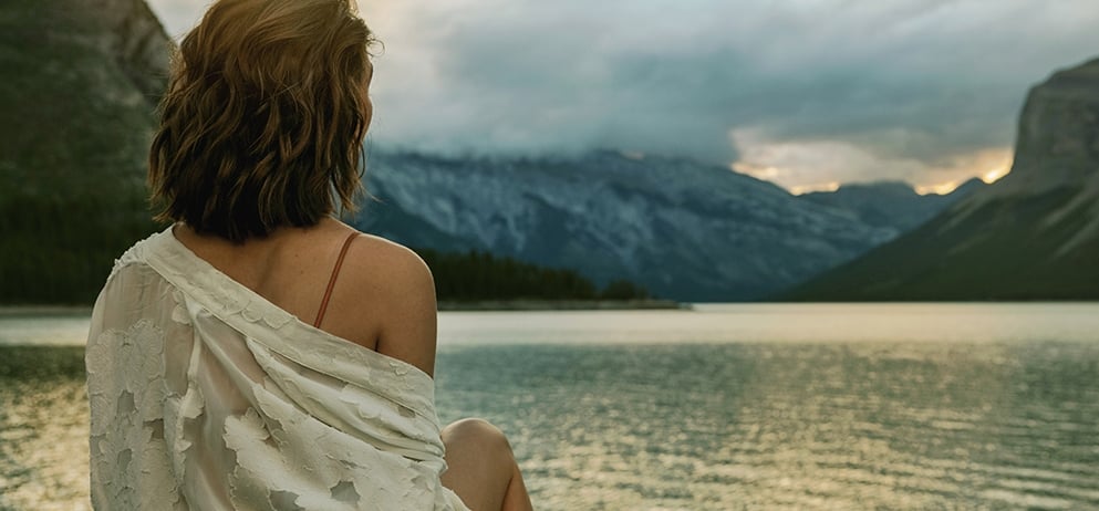 woman with curly hair sits at the edge of lake