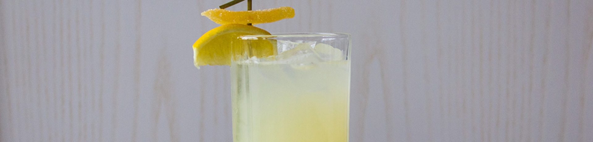 a yellow coloured drink in a tall glass with a lemon garnish