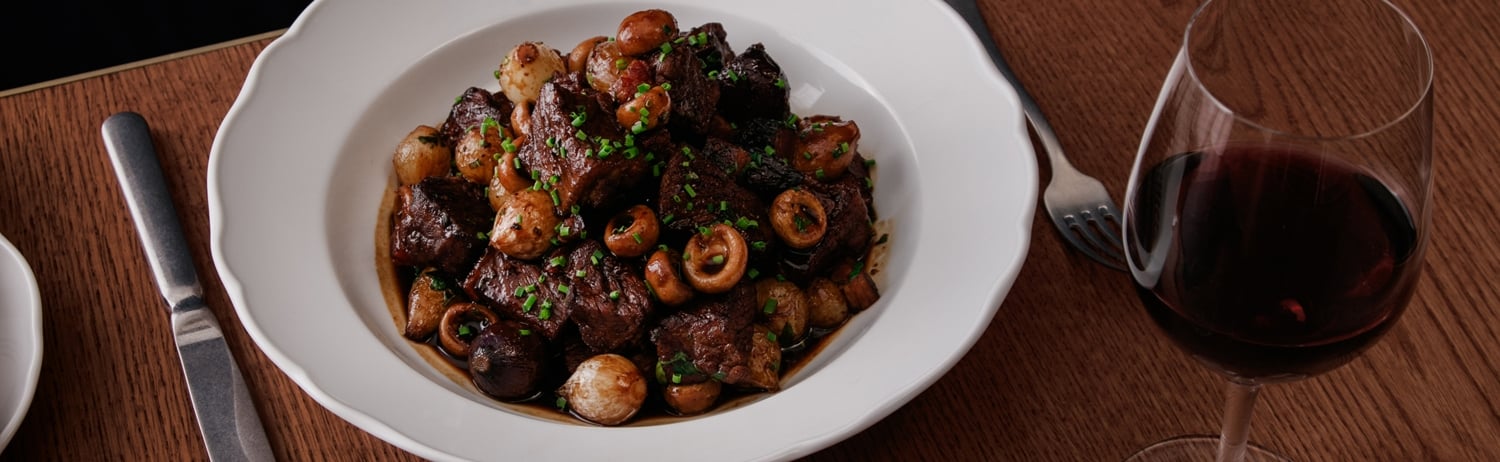 bison bourguignon on white plate sits on wooden table