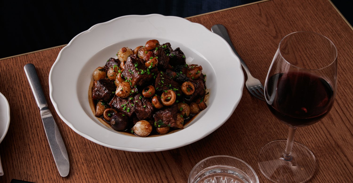 bison bourguignon on white plate sits on wooden table