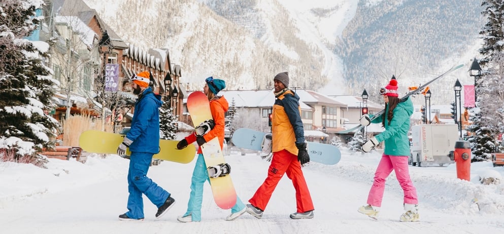 people in colourful winter gear holding snowboards walk outside