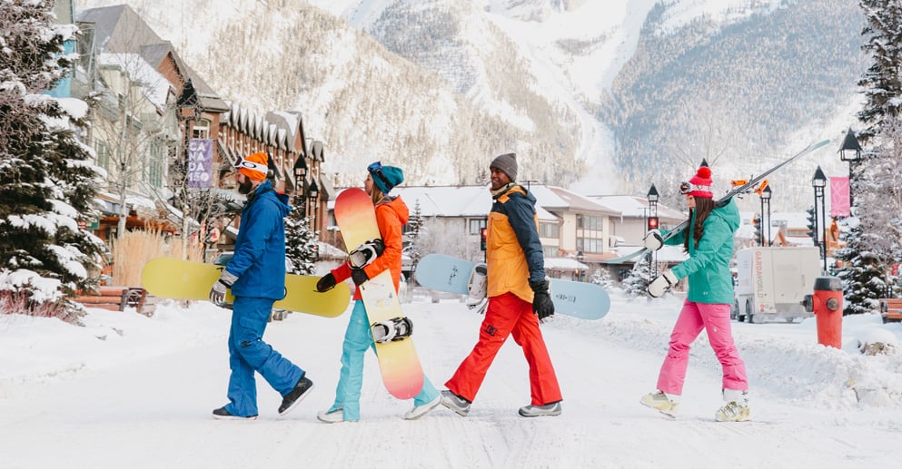 people in colourful winter gear holding snowboards walk outside