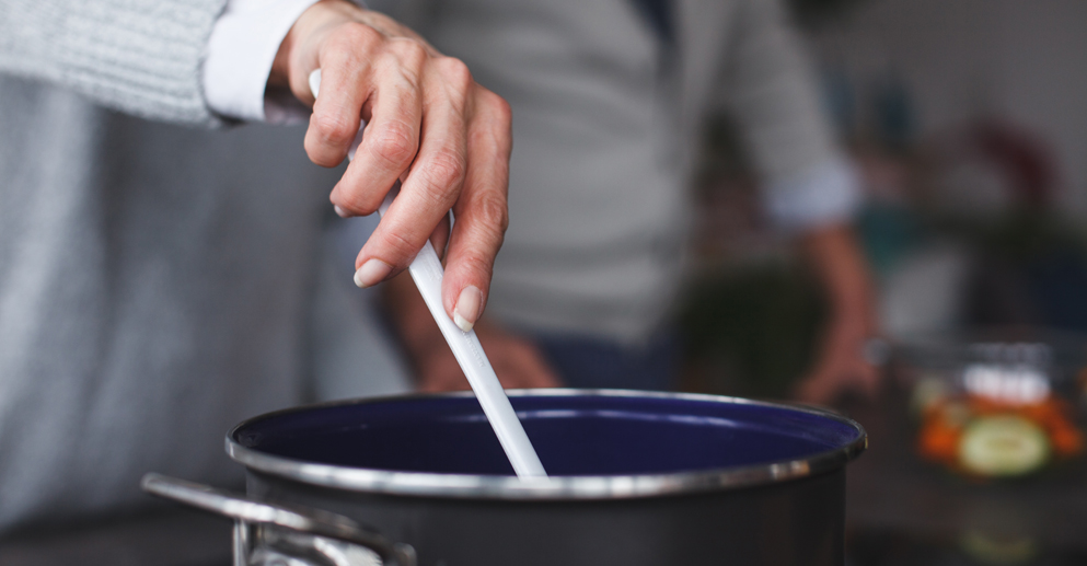 person holding a spoon and mixing a cooking pot.