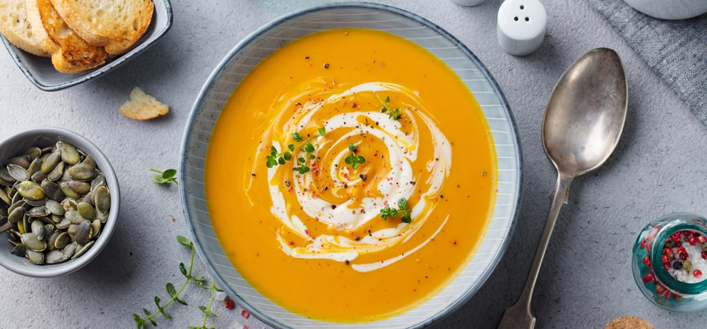 bowl of orange soup with white cream swirls and 
