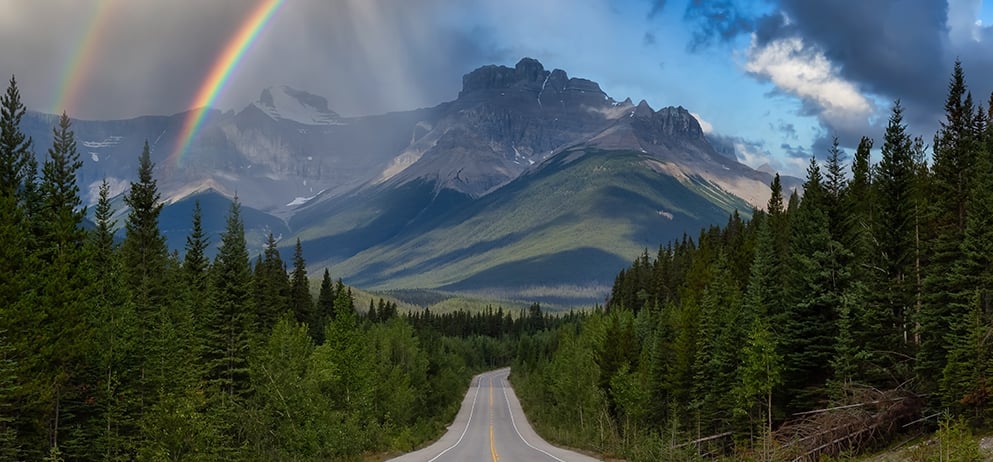 road with a view of the mountains and a rainbow