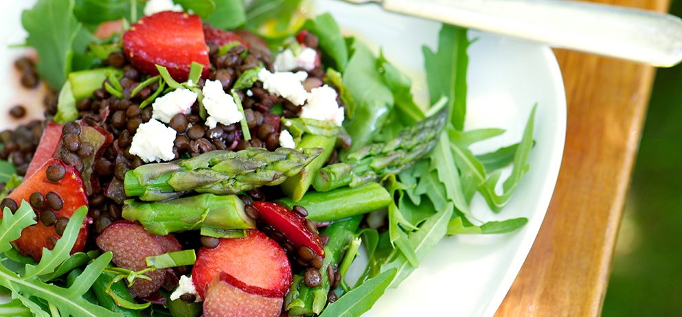 Spring salad with asparagus, rhubarb, strawberries, black lentils, arugula and goat cheese on white plate.