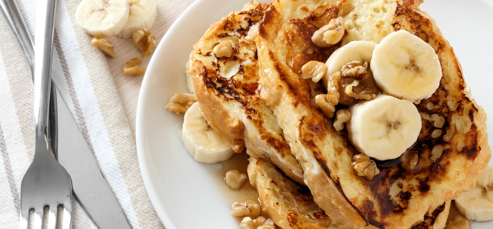 Plate of delicious French toast with bananas, walnuts and dripping maple syrup, overhead view