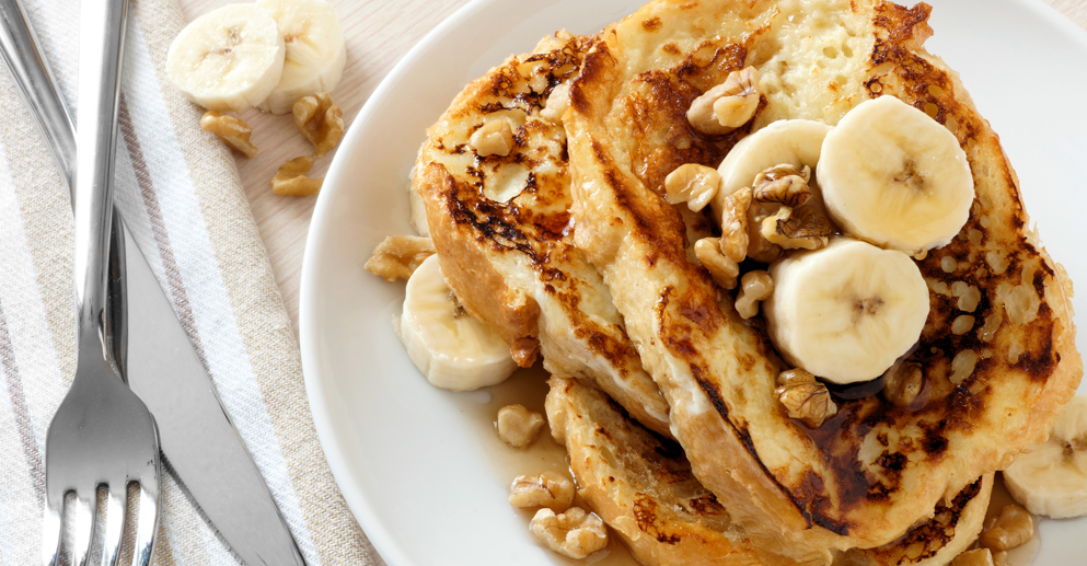 Plate of delicious French toast with bananas, walnuts and dripping maple syrup, overhead view