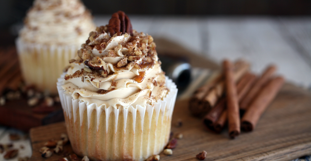 white cupcake with icing covered in nuts sits on wooden table