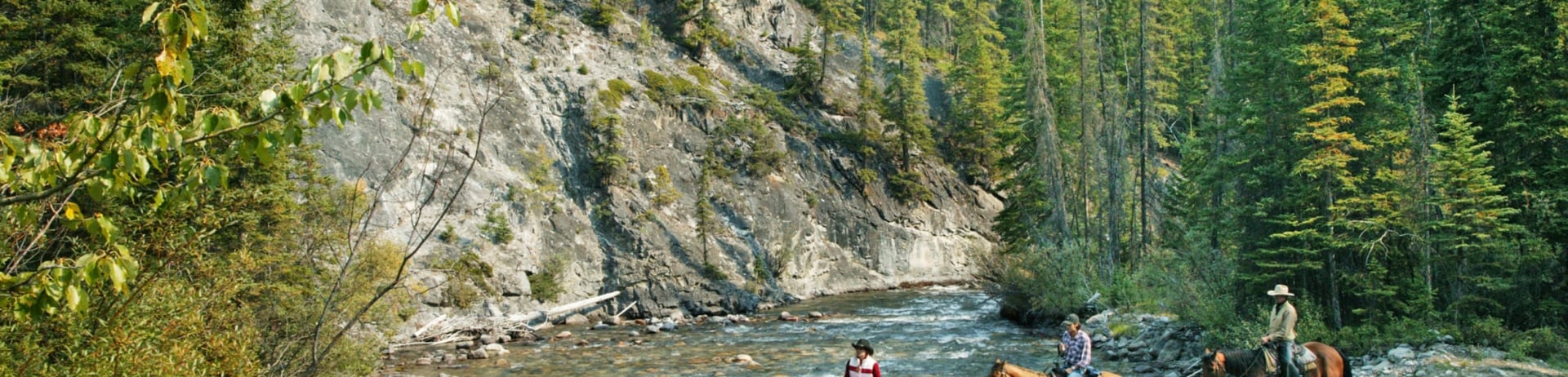 a group of people horse back riding across a river